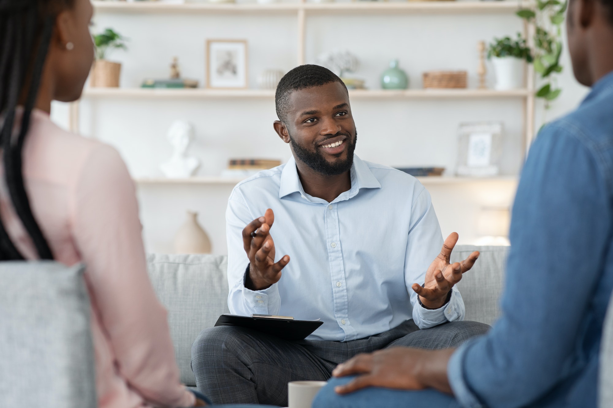 Confident black family counselor talking with married couple, giving advice to spouses